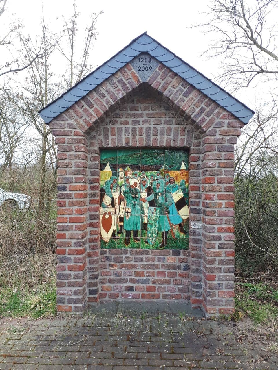 Erinnerungsstätte zum Vertrag von Vinnbrück: Ziegelnische mit Schieferdach und der Inschrift „1284–2009“, darin das Keramikbild mit Rittern.