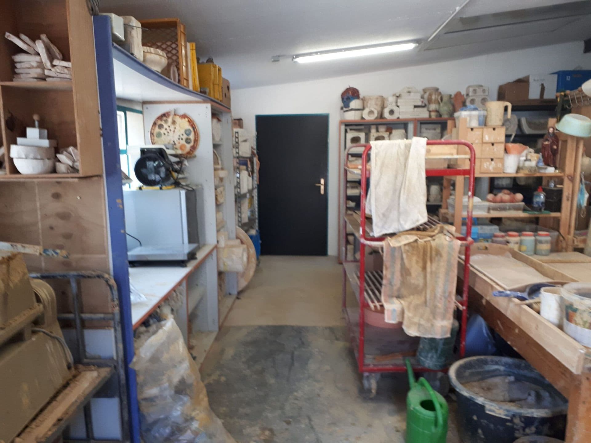 Blick in den Werkstattraum mit Regalen, Arbeitstisch und einer offenen Tür im Hintergrund.