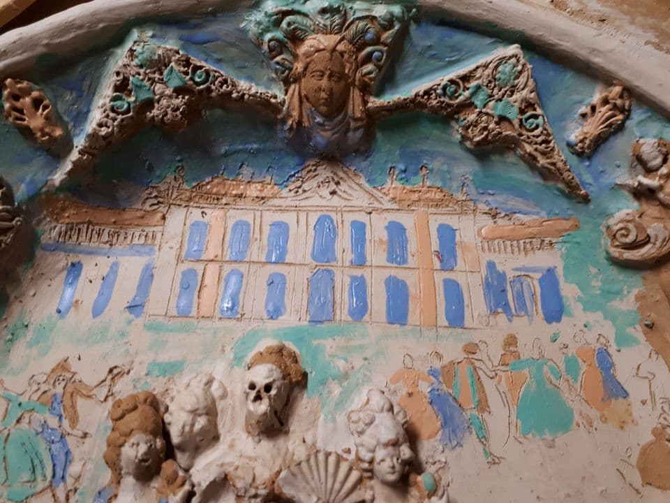 Der Teller mit Engobe bemalt: ein Schloss mit blauen Fenstern, darüber eine Maske zwischen Ornamenten, davor die Figurengruppe mit Skelett und gemalte tanzende Paare.