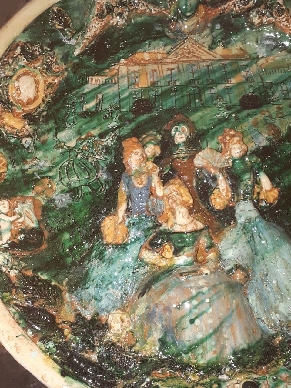 Der glasierte Teller in der Schrägansicht, Schloss und Figurengruppe in Grün-, Braun- und Blautönen.