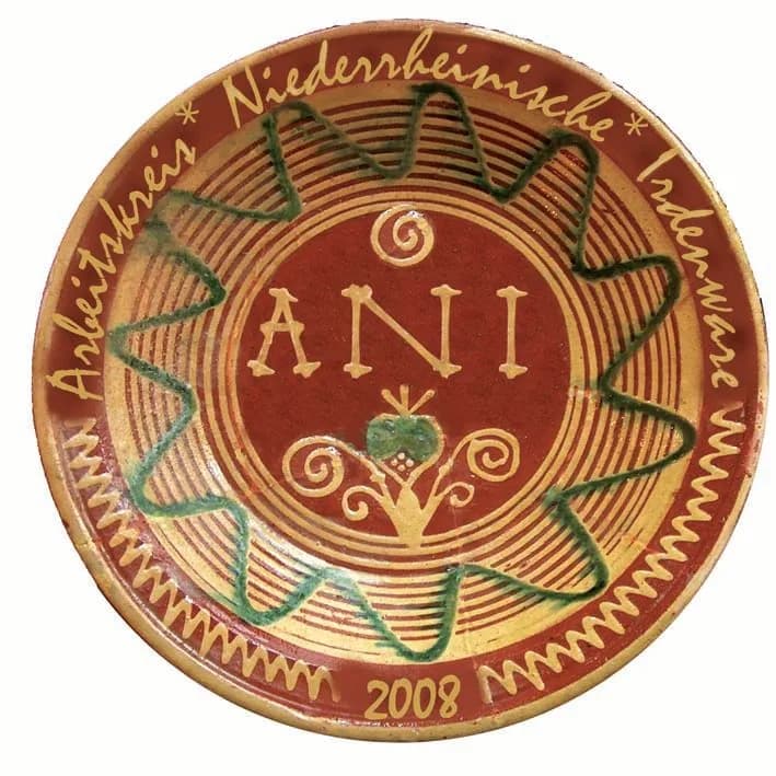 Teller mit den Buchstaben ANI im Spiegel, grünem Wellenband und dem Schriftzug „Arbeitskreis Niederrheinische Irdenware“, Jahreszahl 2008.