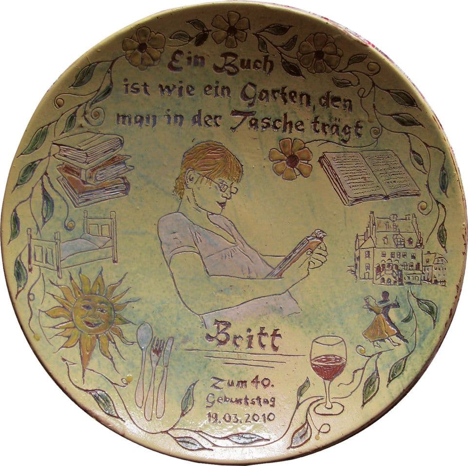Geburtstagsteller zum 40.: lesende Frau mit Buch, Weinglas und Blumen, Spruch über das Buch als Garten in der Tasche, Datum 2010.