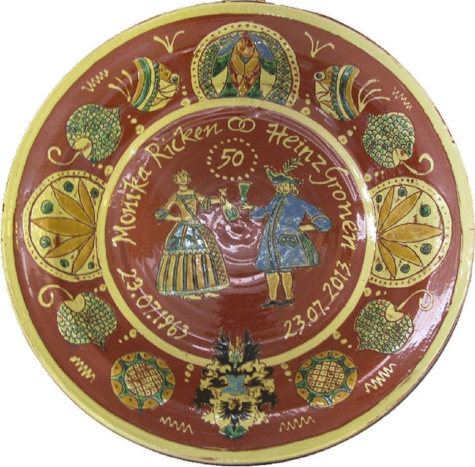 Wandteller zur Goldhochzeit: Brautpaar in historischer Tracht mit Namen und der Zahl 50 im Spiegel, außen ein Kranz aus Blüten- und Wappenmotiven.