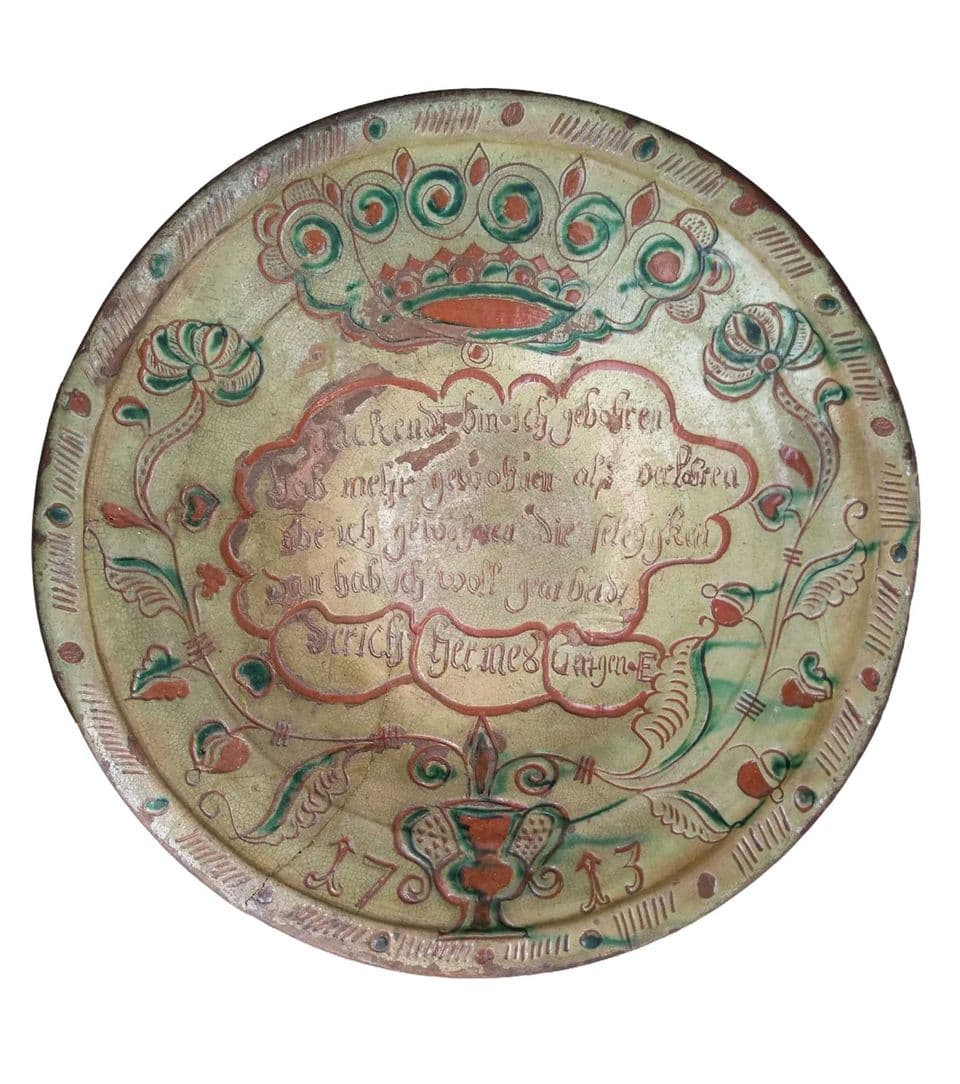 Tönisberger Teller von 1713 mit Schriftkartusche in der Mitte, grüne und rote Malhornranken am Rand.