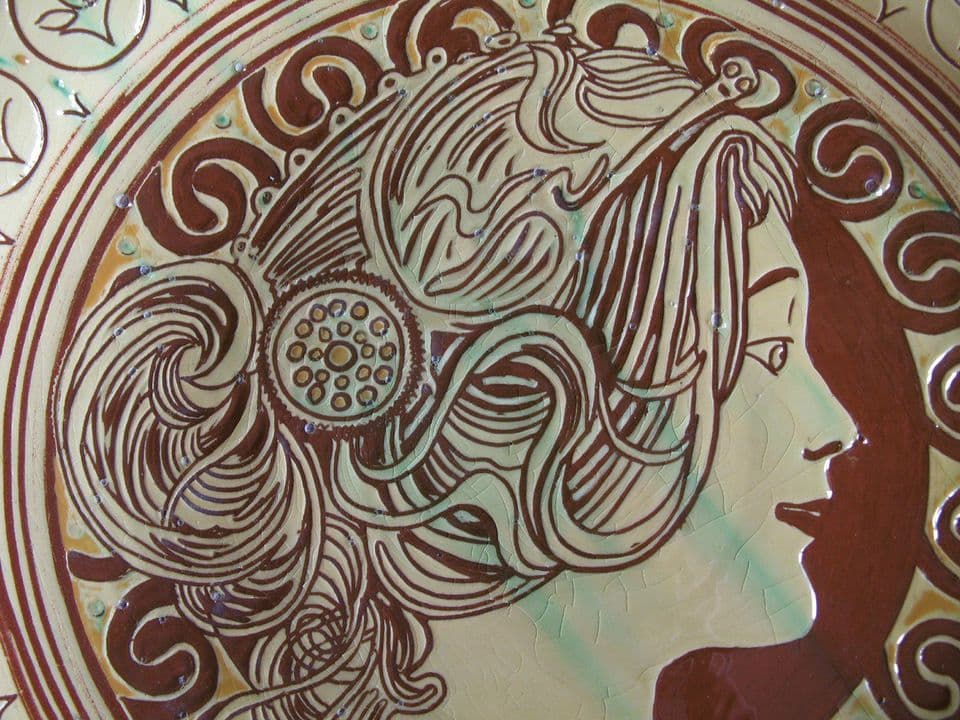 Detail eines Wandtellers: Frauenprofil mit kunstvoll gewundenem Haar in Dunkelbraun auf hellem Grund.