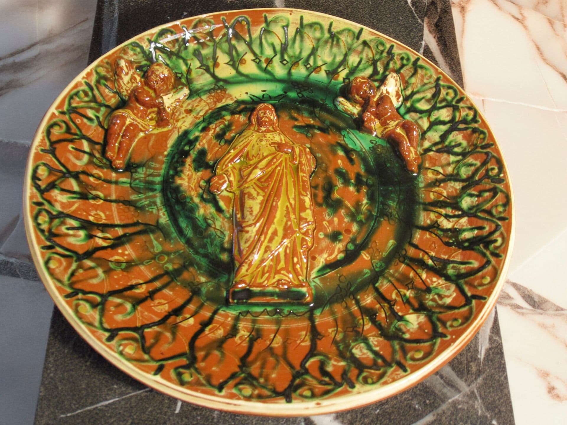 Reliefteller mit stehender Christusfigur im Spiegel, Rand mit Strahlenkranz in Grün und Braun.