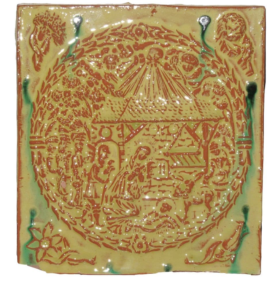 Relieffliese mit Krippenszene unter einem Stern im Kranz, rotbraune Linien unter gelber Glasur mit grünen Läufen, in den Ecken Blüten und Figuren.