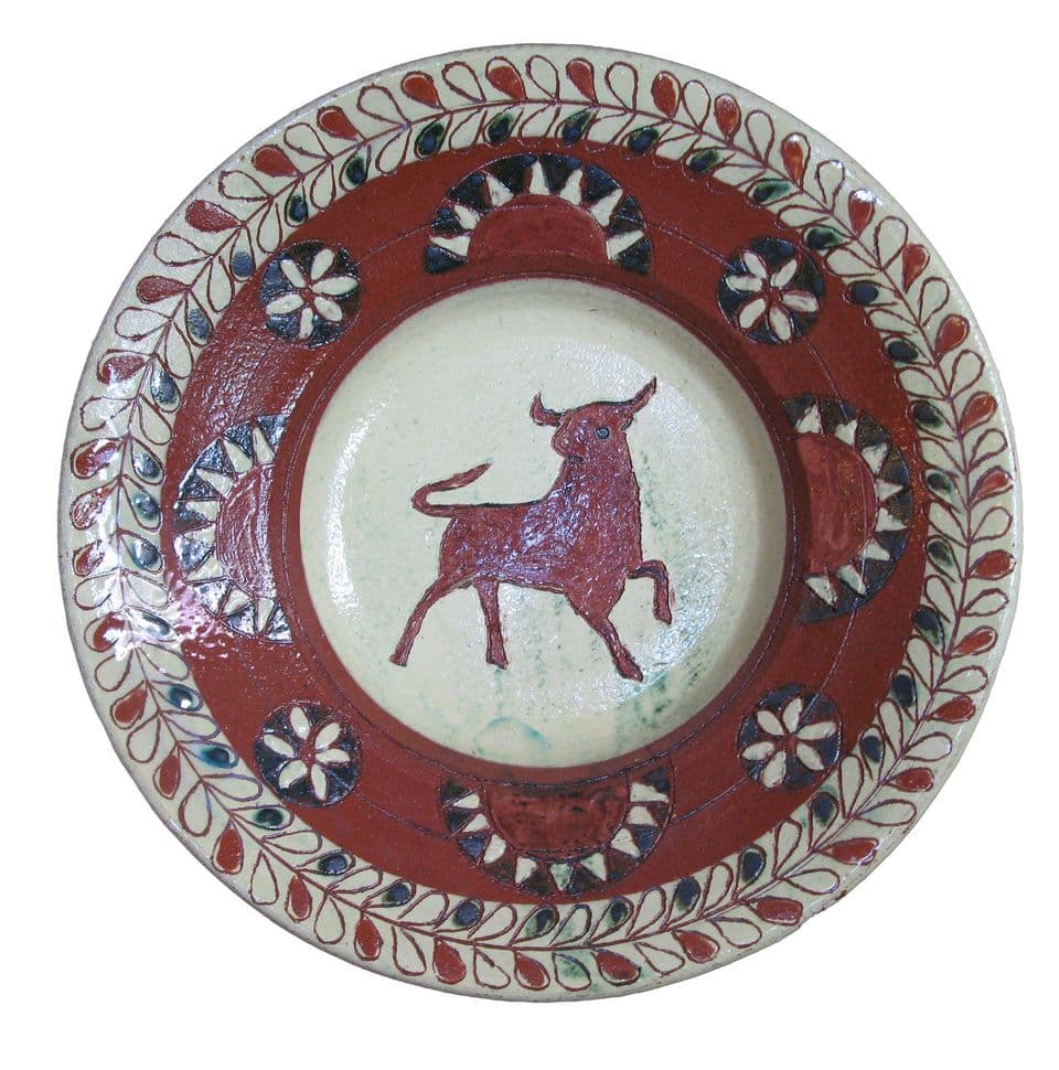 Teller mit braunem Stier auf hellem Spiegel, Rand mit roten Blüten und Zacken in Weiß und Braun.