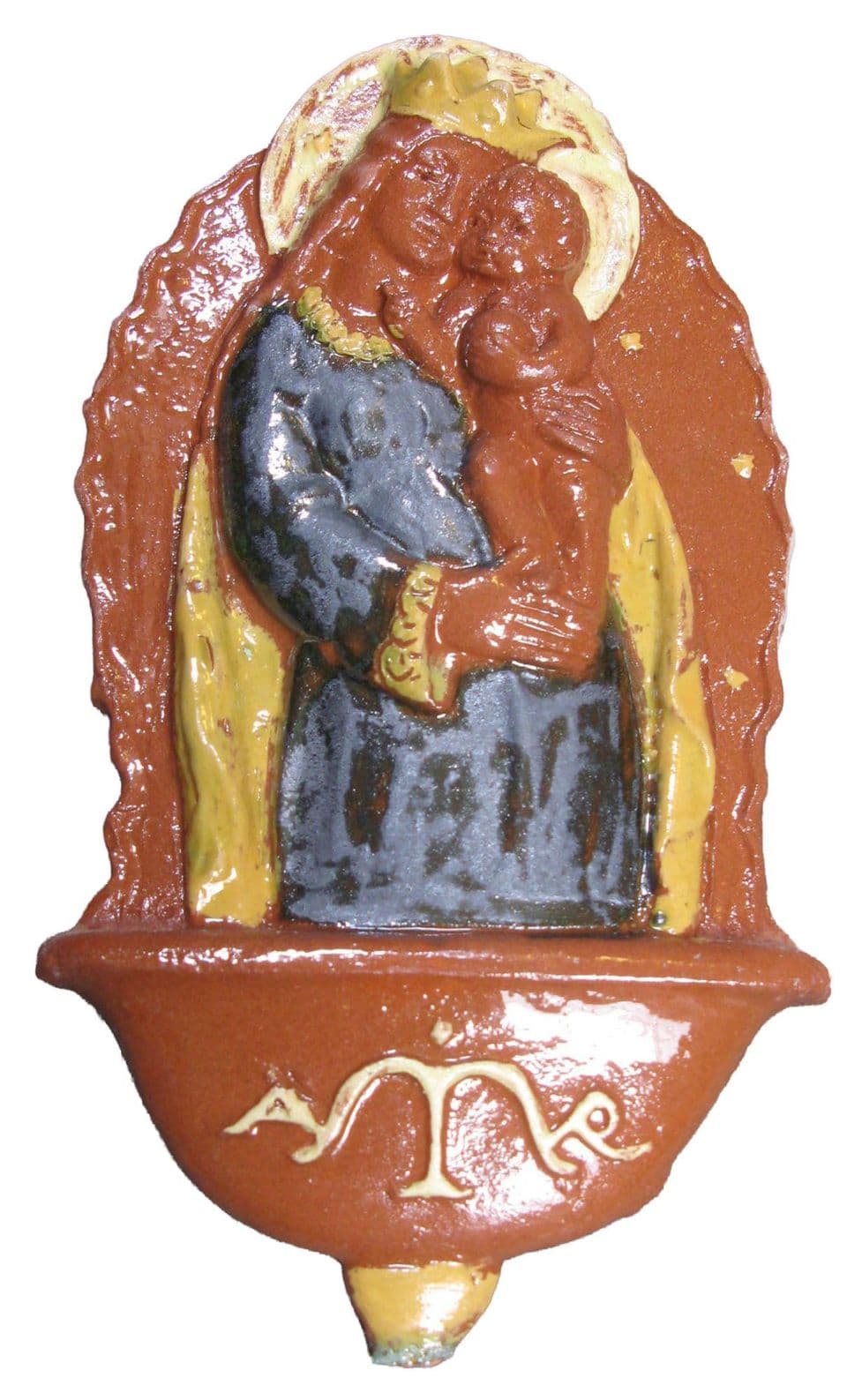 Weihwasserbecken als Wandplakette: gekrönte Maria in blaugrauem Gewand mit dem Kind im Arm, darunter das rotbraune Becken mit hellem Monogramm.